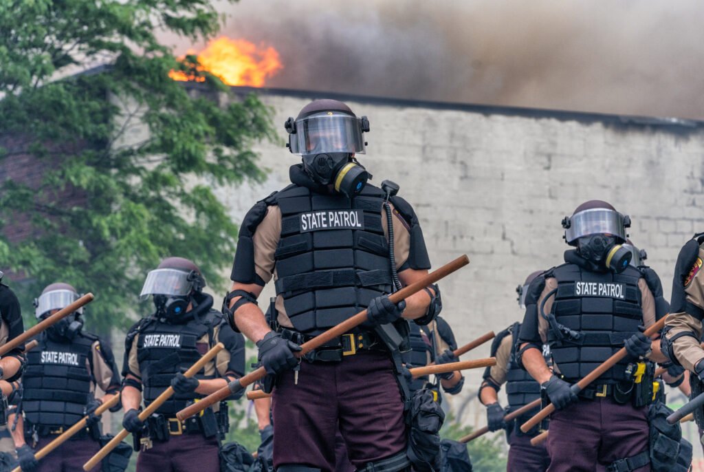 Minnesota State Patrol troopers stand in formation, wearing riot gear and holding wooden batons, at Minnehaha Avenue and 27th Avenue South near the Minneapolis Police Department's 3rd Precinct, as the Minneapolis Fire Department battles blazes at Lake Street businesses, following the publication of a video showing a white Minneapolis police officer kneeling on the neck of George Floyd, a handcuffed and unarmed Black man, killing him.