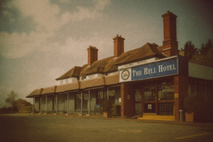 A grainy, vintage-style photograph of The Bell Hotel, a red-brick building with multiple chimneys and a pitched roof. The hotel’s blue sign is visible above the entrance, while the windows and forecourt appear muted and faded, giving the image a 1968 protest-poster aesthetic.
